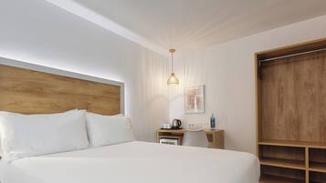 Une chambre avec un grand lit, une tête de lit en bois, une table de chevet avec une bouilloire, une petite chaise et une armoire en bois.
