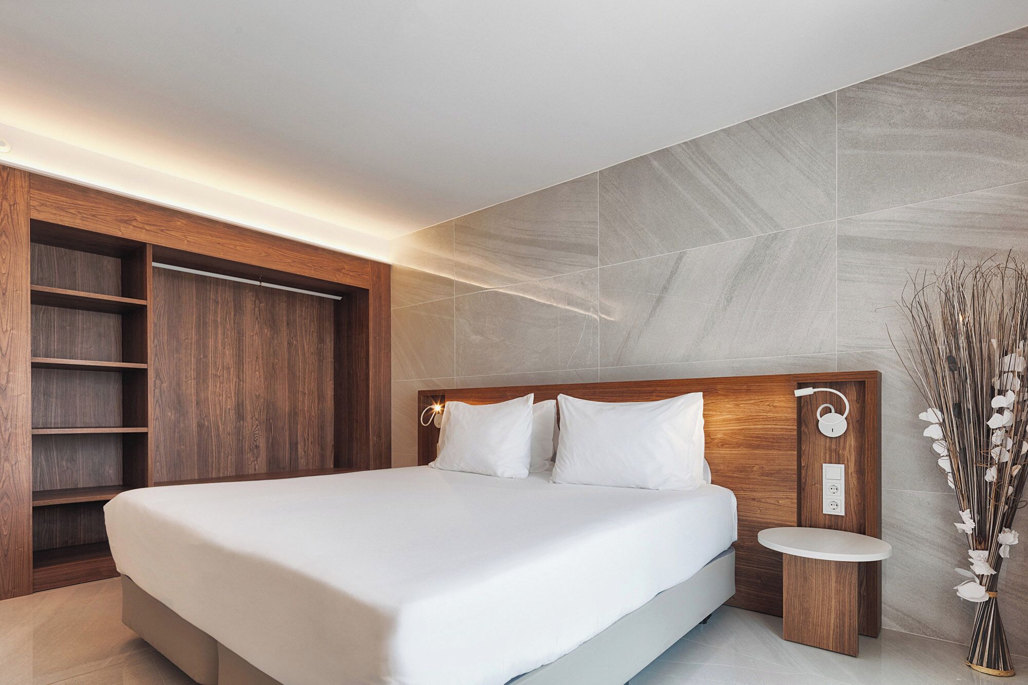 Un dormitorio moderno con una cama grande, cabecera de madera, estanterías empotradas y una mesita de noche con lámpara.