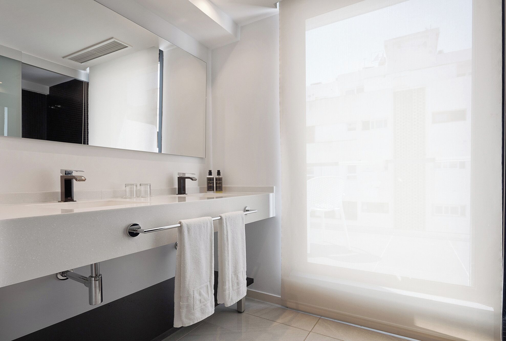 Un baño moderno con un espejo grande, una encimera blanca y un perchero para toallas.