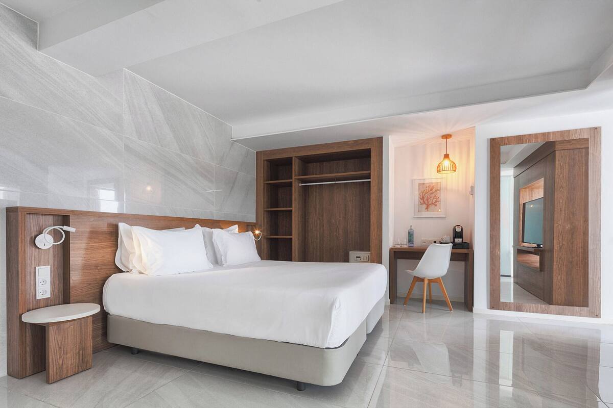 Une chambre moderne avec un grand lit, une tête de lit en bois, des tables de chevet, un bureau et une chaise.