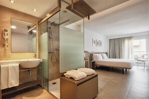A modern hotel room with a glass-enclosed shower, a large bed, a bedside table with towels, a vanity with a sink, and a large mirror. - Eurostars Puerto de Ibiza (Ibiza Town)