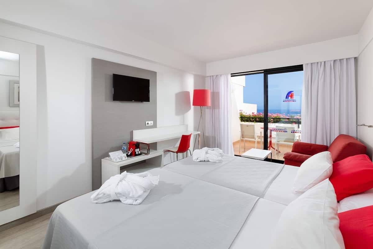 Ein Hotelzimmer mit Bett, Schreibtisch, Stuhl, Fernseher und einem Balkon mit Aussicht.