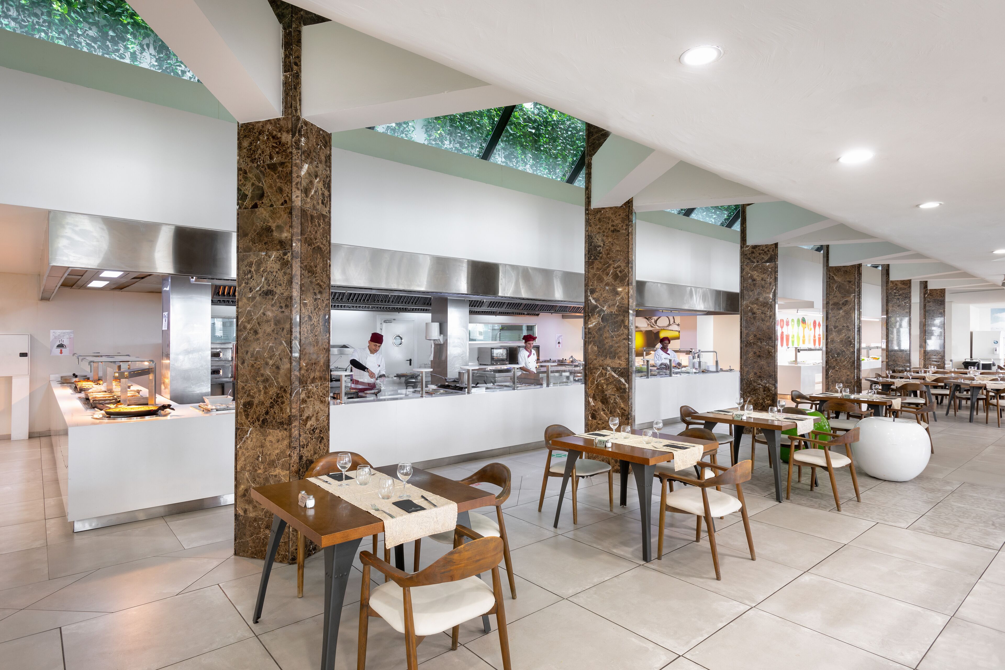 A modern restaurant with marble pillars, a central kitchen, and a variety of seating options.