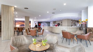 Un moderno vestíbulo de hotel con zonas de estar, un bar y un gran mural de un atardecer.