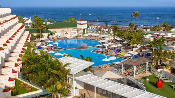 Un resort con una gran piscina, tumbonas y vistas al océano.