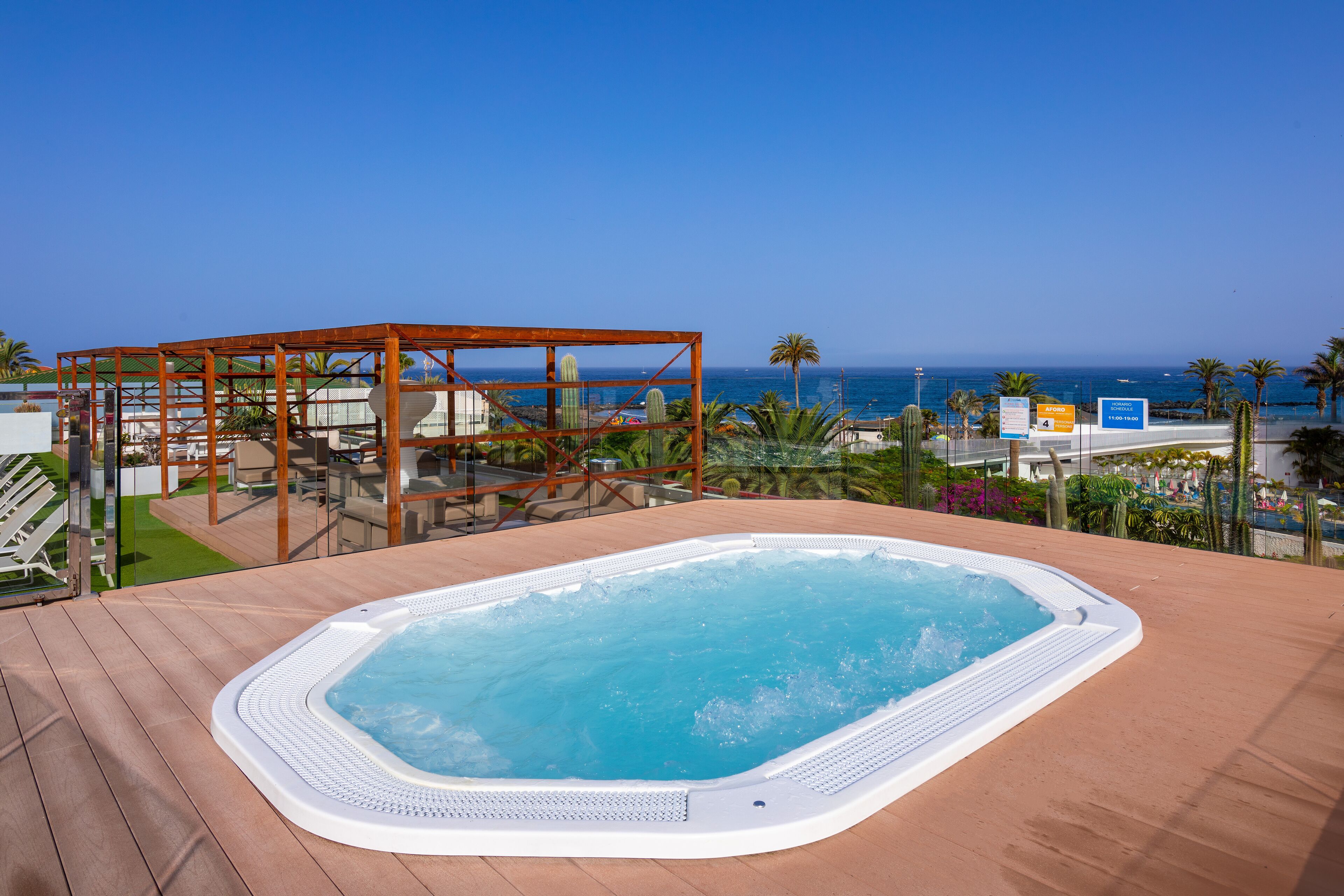 Un jacuzzi en una terraza de madera con vista al océano y palmeras.