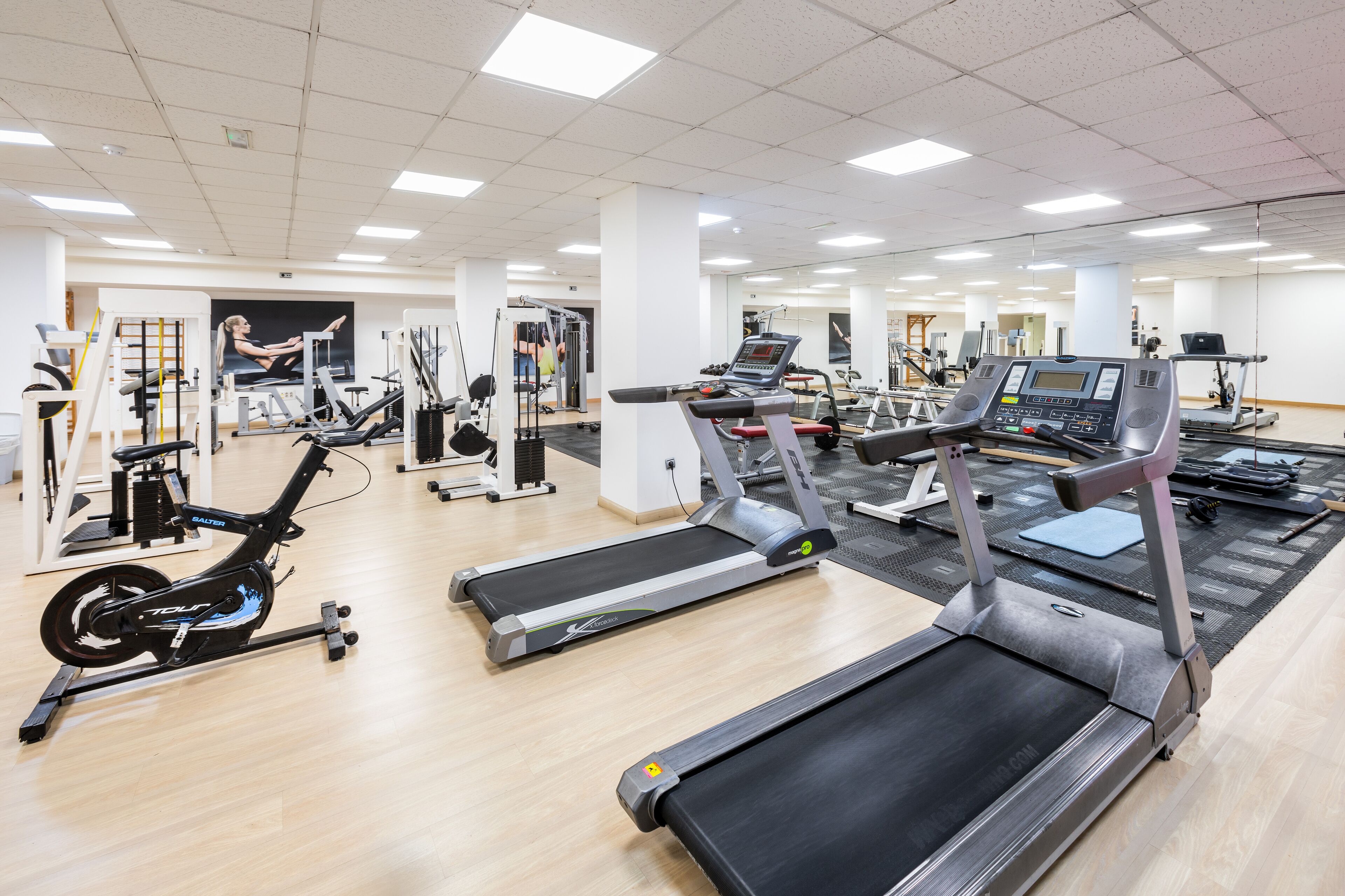 Uma academia com esteiras, bicicletas ergométricas e diversos equipamentos de exercícios.