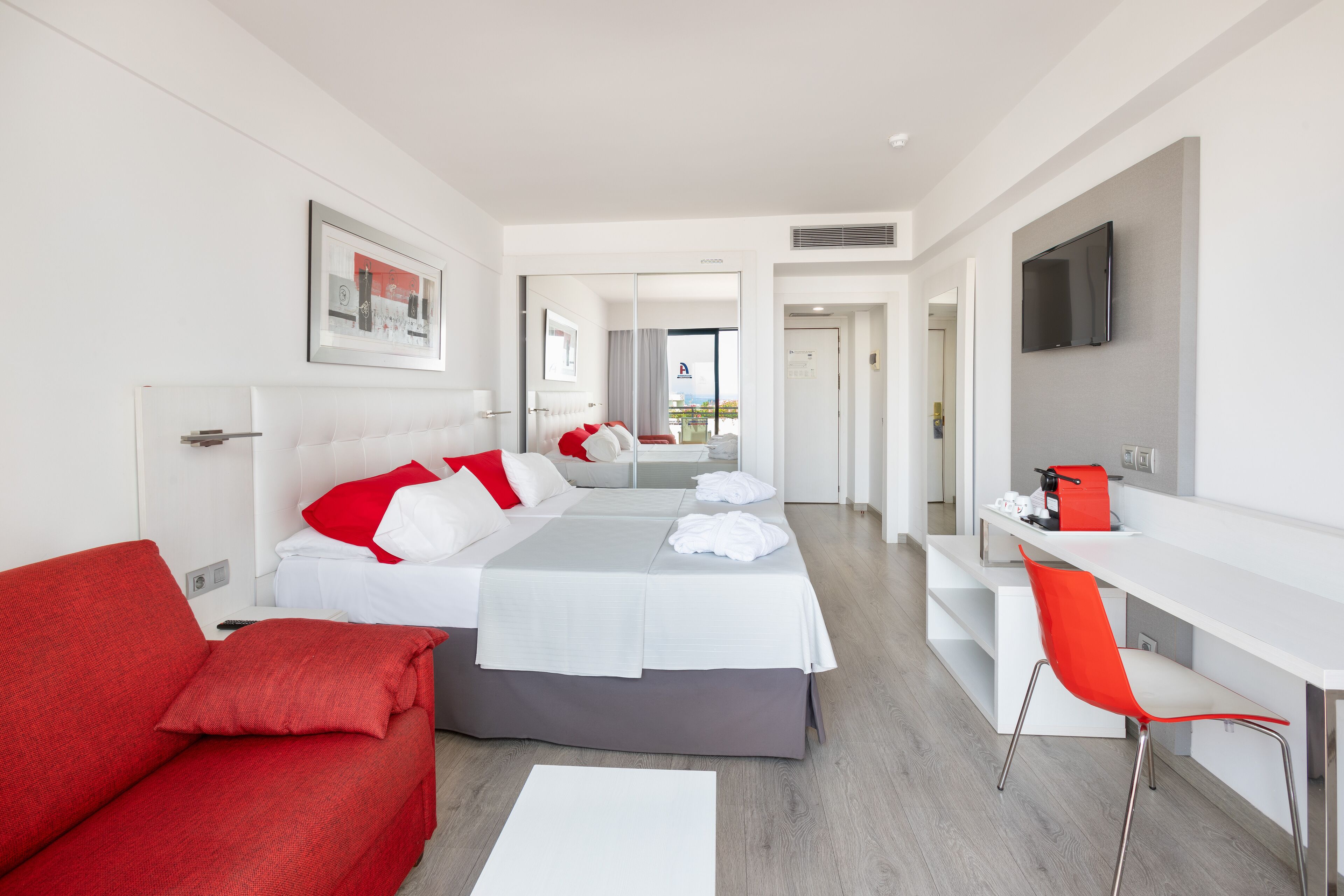 Camera d'albergo moderna con un letto, una poltrona rossa, una scrivania e una TV.