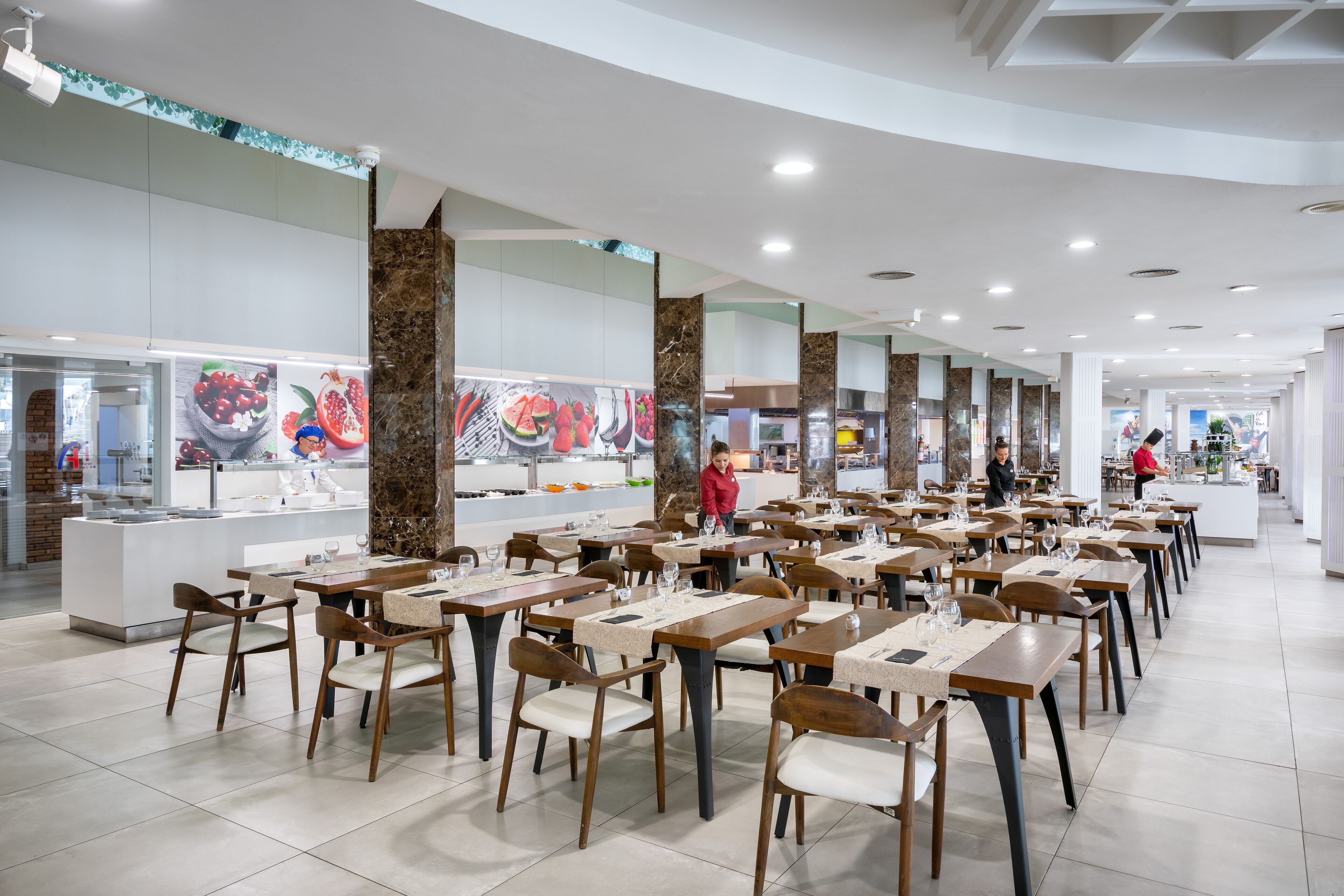 Ein geräumiges Restaurant mit mehreren Tischen und Stühlen, einem zentralen Servicebereich und einem modernen Ambiente.