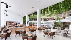 Un amplio espacio interior con diversas disposiciones de asientos, incluyendo mesas redondas y sillas, y una escalera central.
