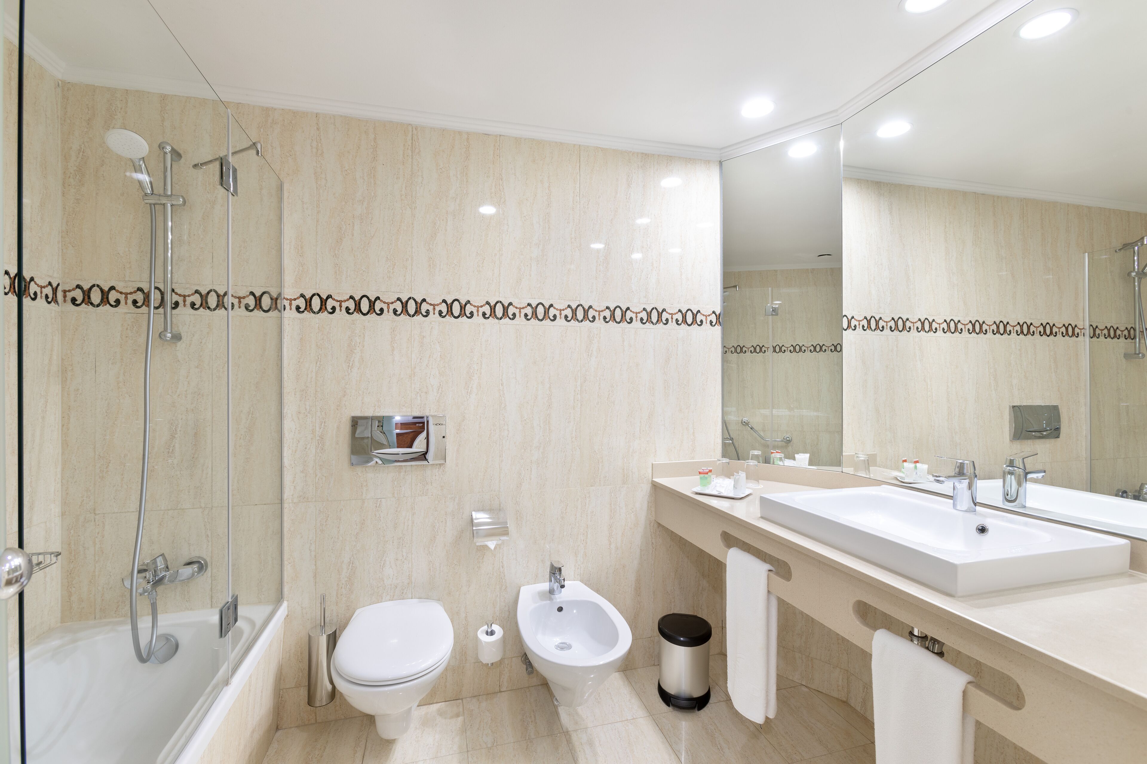 Un baño moderno con bañera, ducha, inodoro, bidé y lavamanos con un espejo grande.