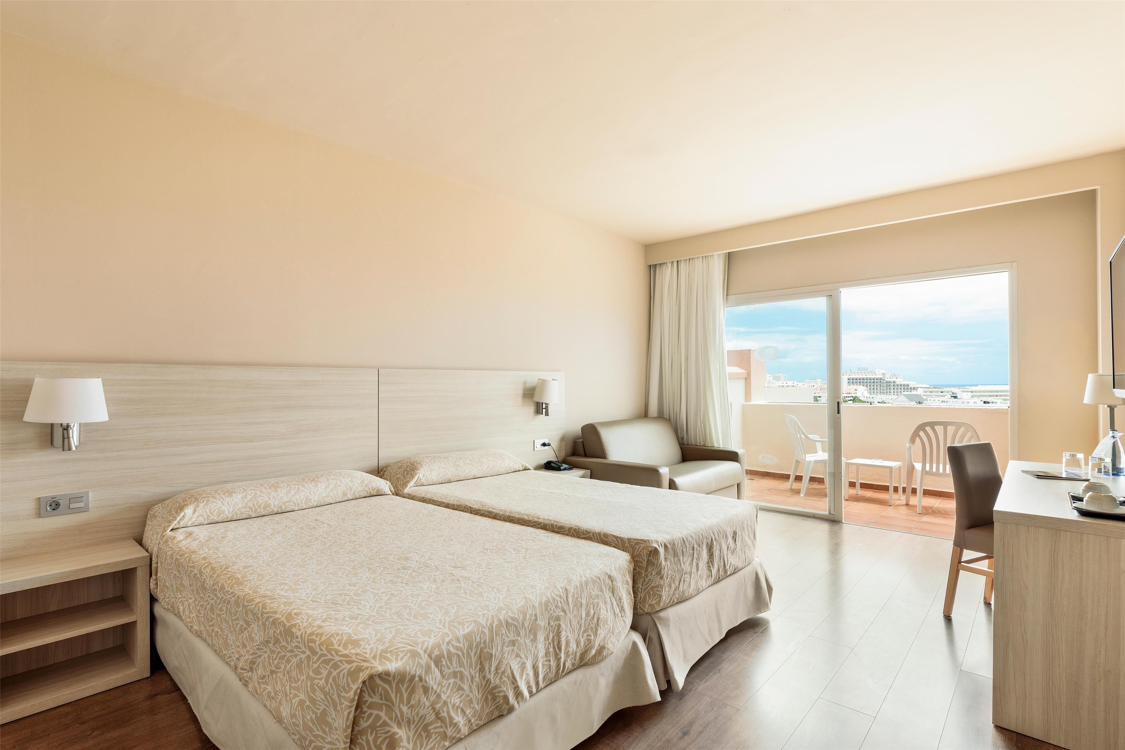 Een hotelkamer met twee bedden, een bureau, een stoel en een balkon met uitzicht.