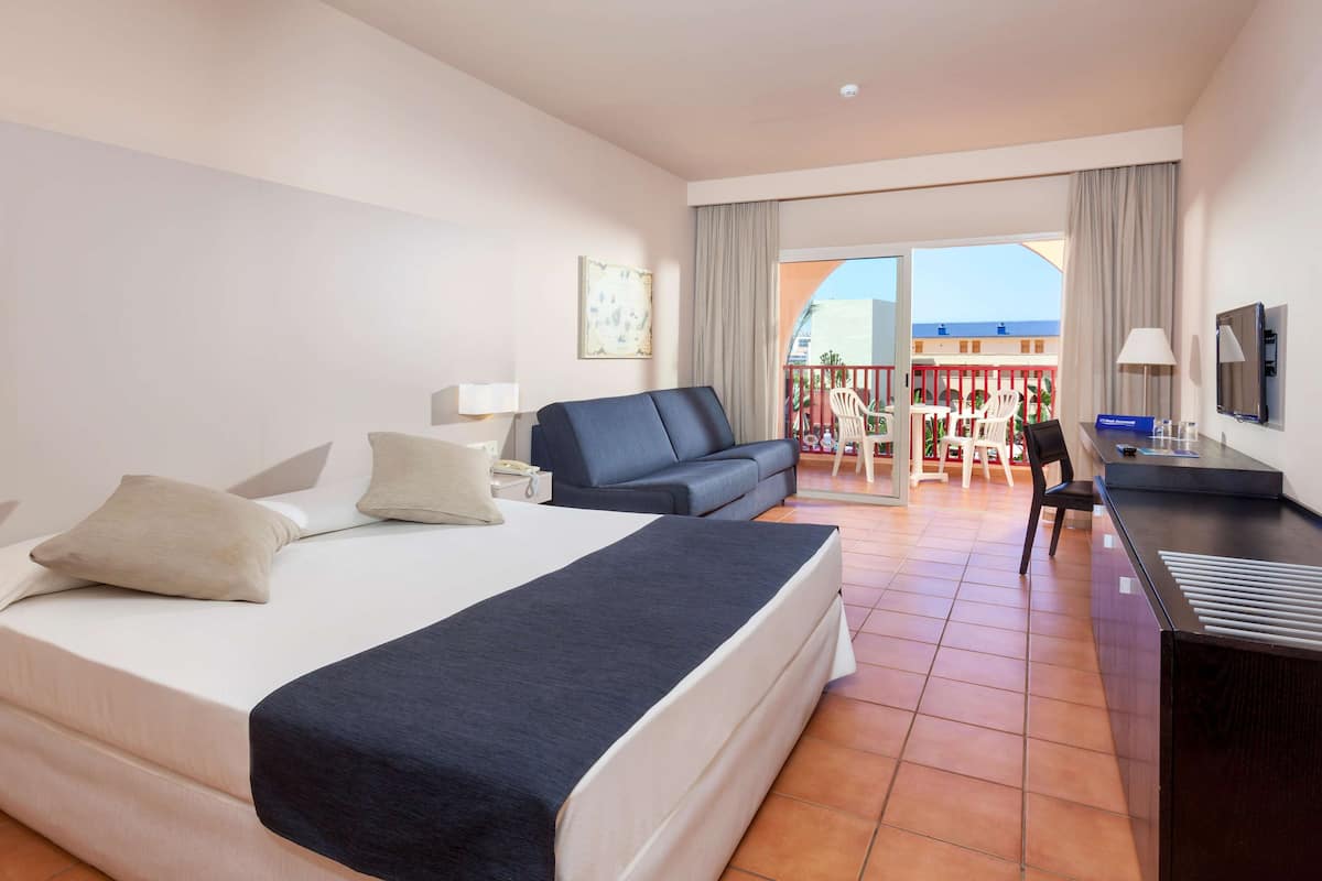 Habitación de hotel con cama, escritorio, silla, sofá y balcón con vistas.