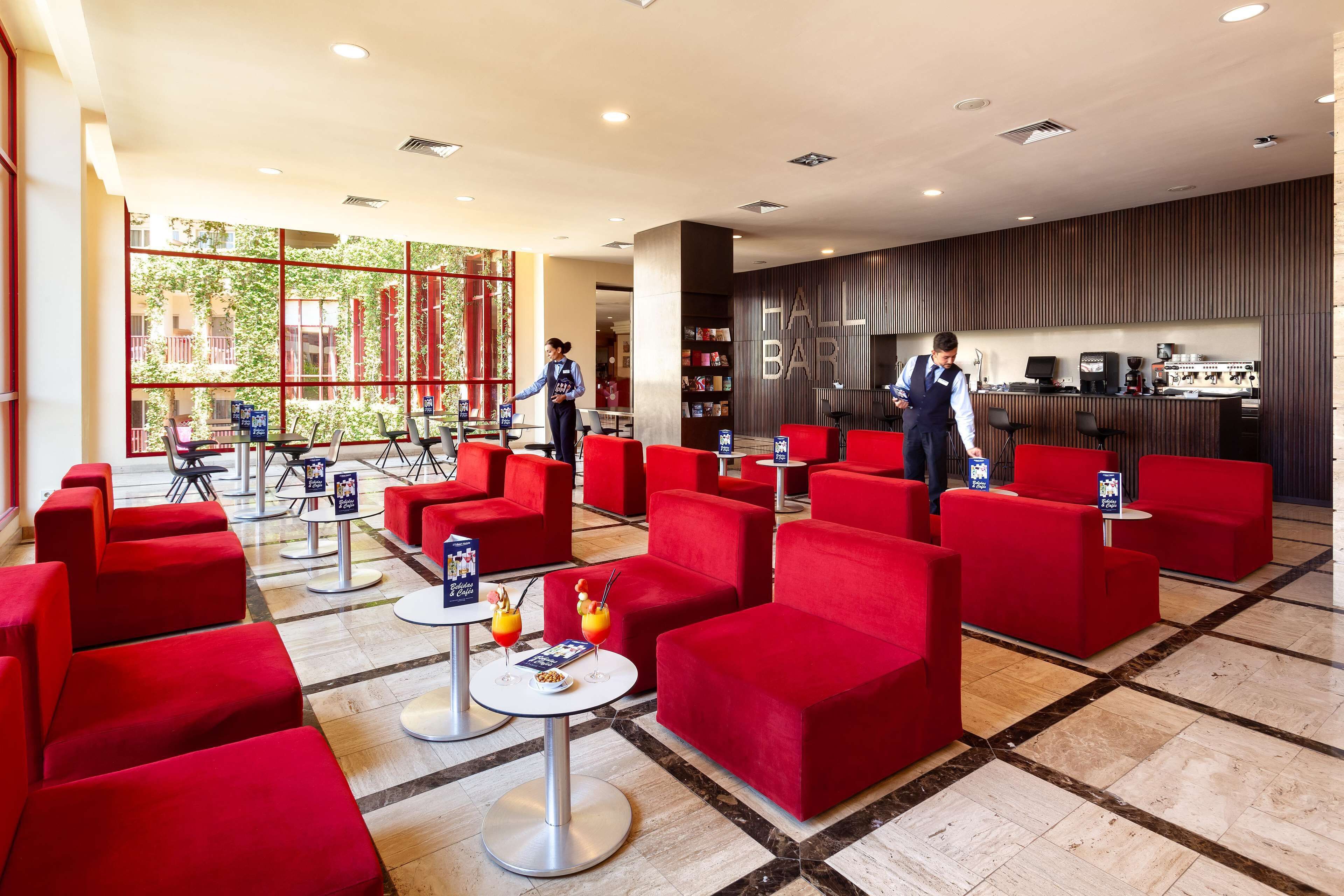Un hall d’hôtel avec des sièges rouges, un comptoir d’accueil et une vue sur l’extérieur.