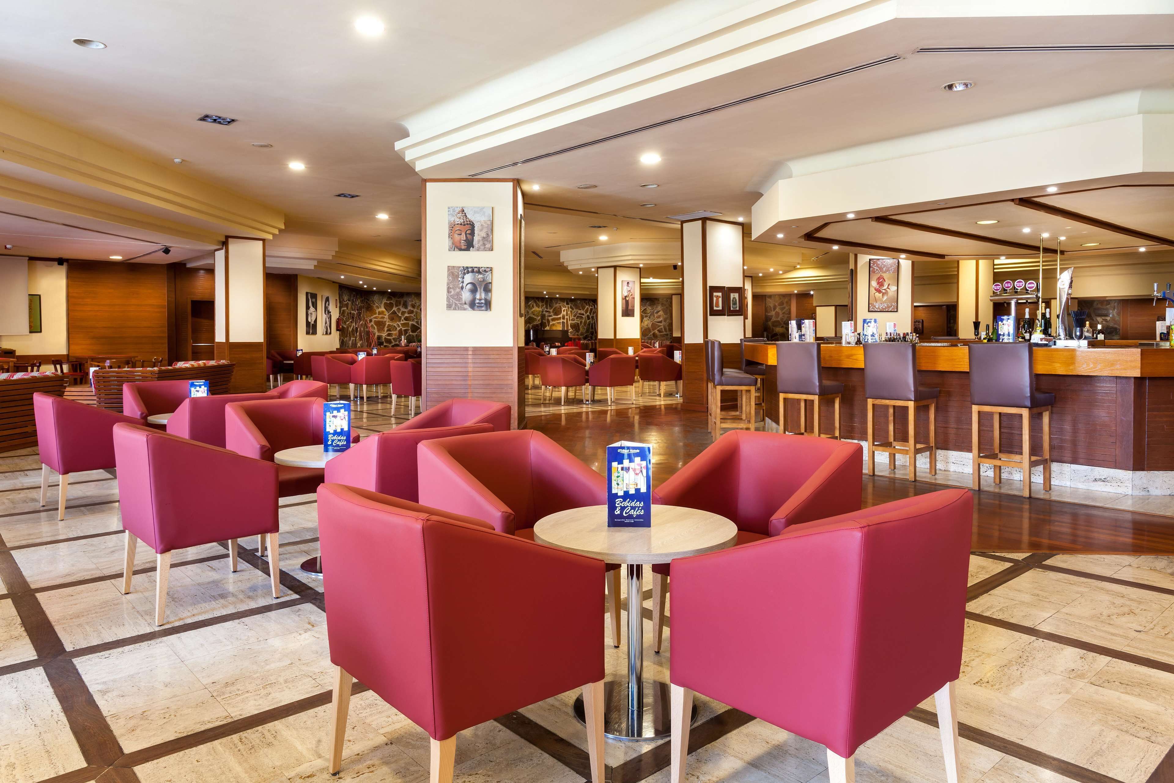 Un vestíbulo amplio con asientos rojos, una zona de bar y un mostrador de recepción.