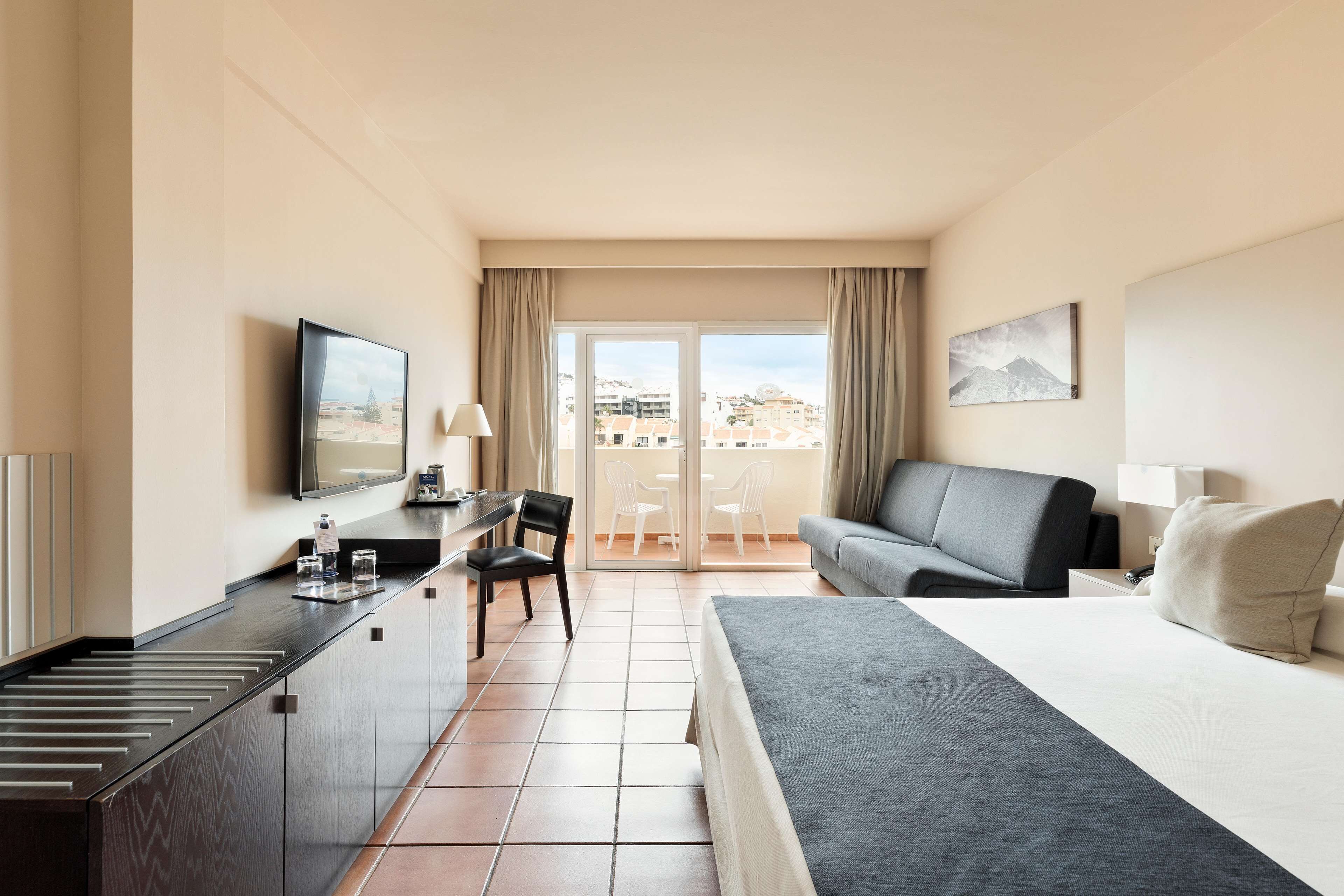 Une chambre d’hôtel comprenant un lit, un bureau avec une chaise, un canapé, une télévision et un balcon avec vue sur les bâtiments.