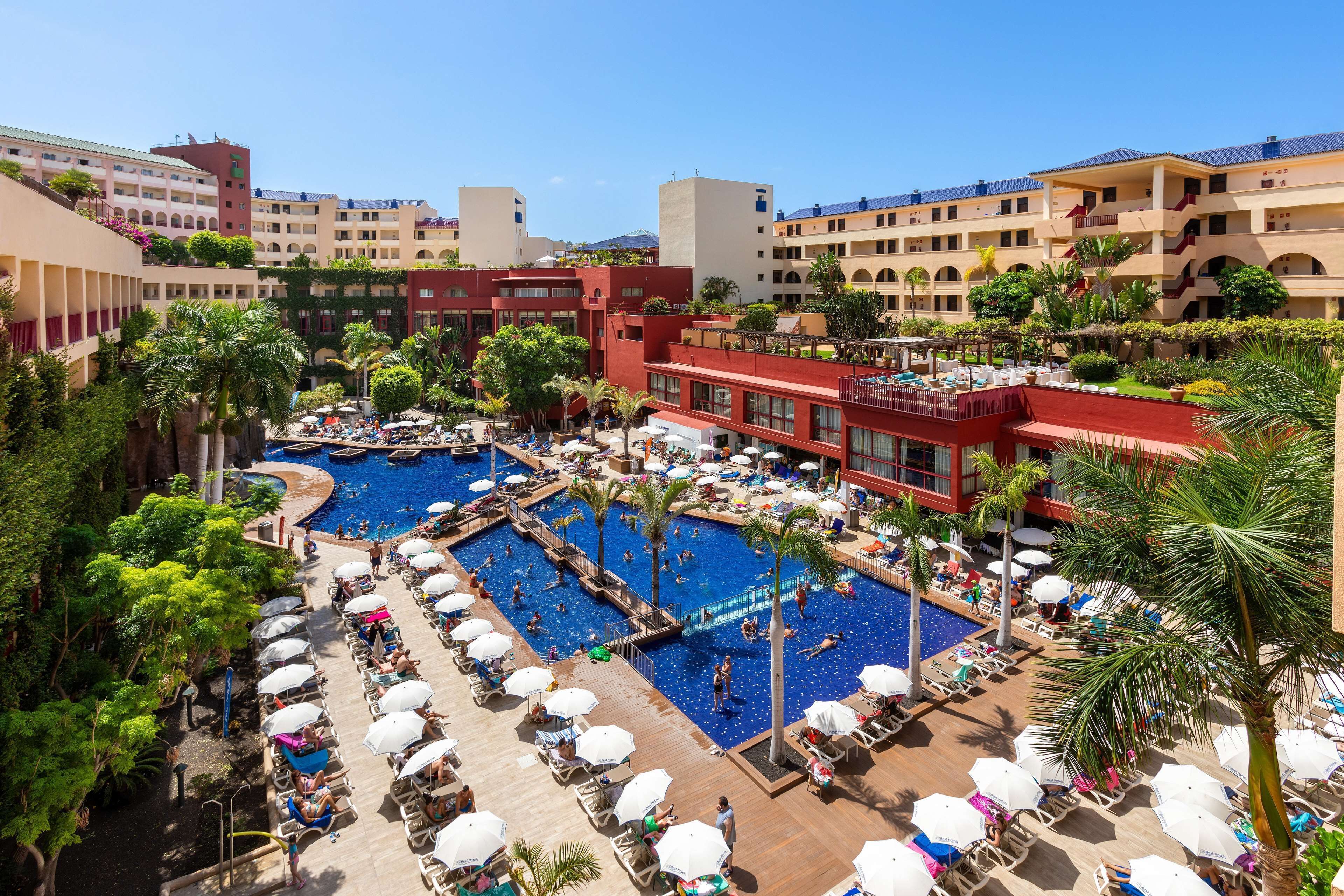 Un hotel con varias piscinas, tumbonas y palmeras.