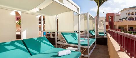 A rooftop pool area with sun loungers and a palm tree.