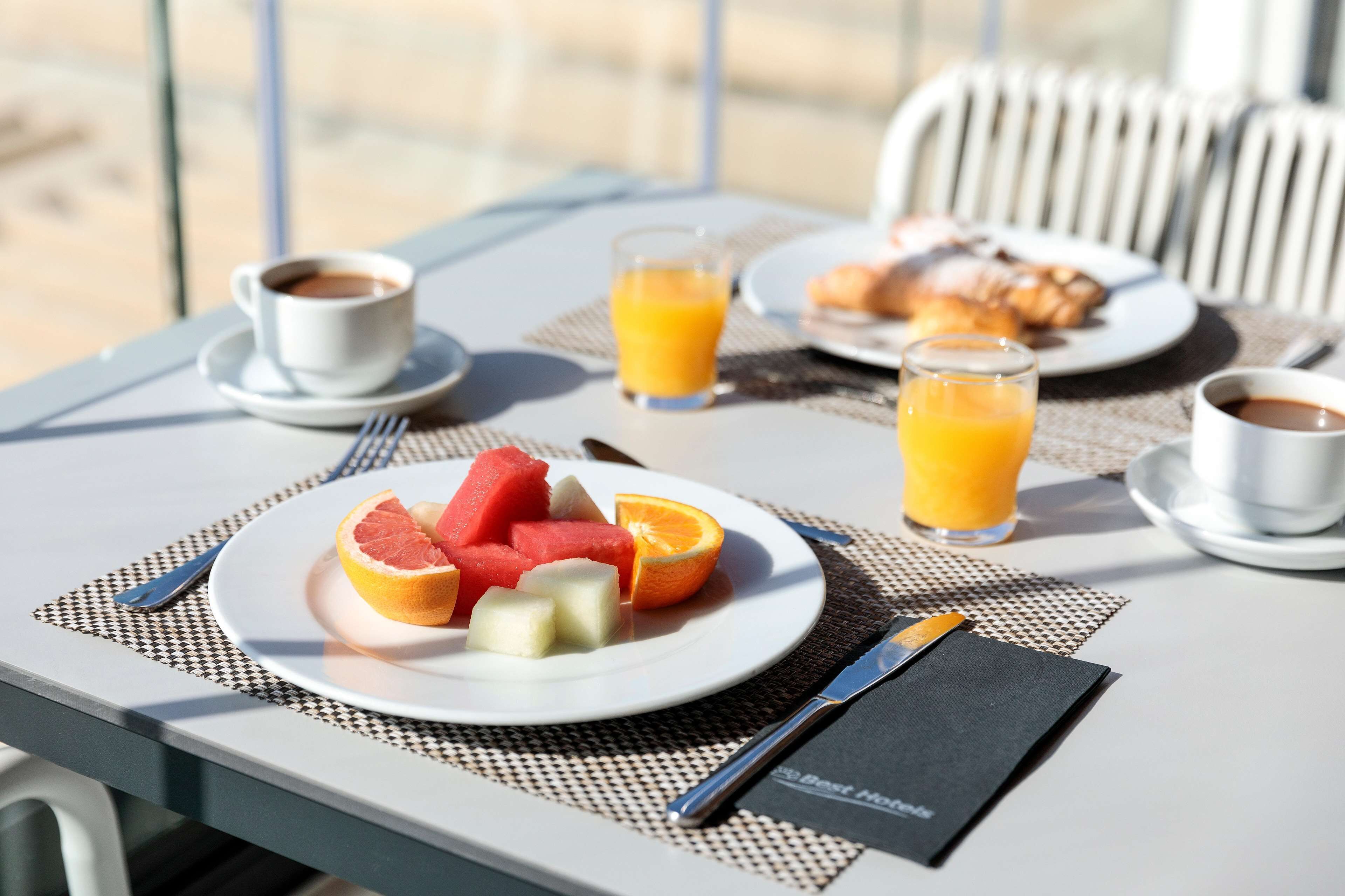 Een ontbijtsetting met een fruitschaal, twee glazen sinaasappelsap en een kop koffie op een tafel.