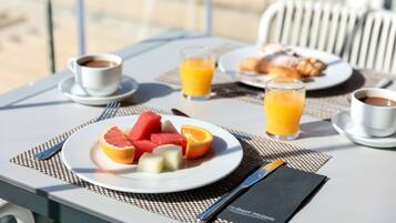 Een ontbijtsetting met een fruitschaal, twee glazen sinaasappelsap en een kop koffie op een tafel.