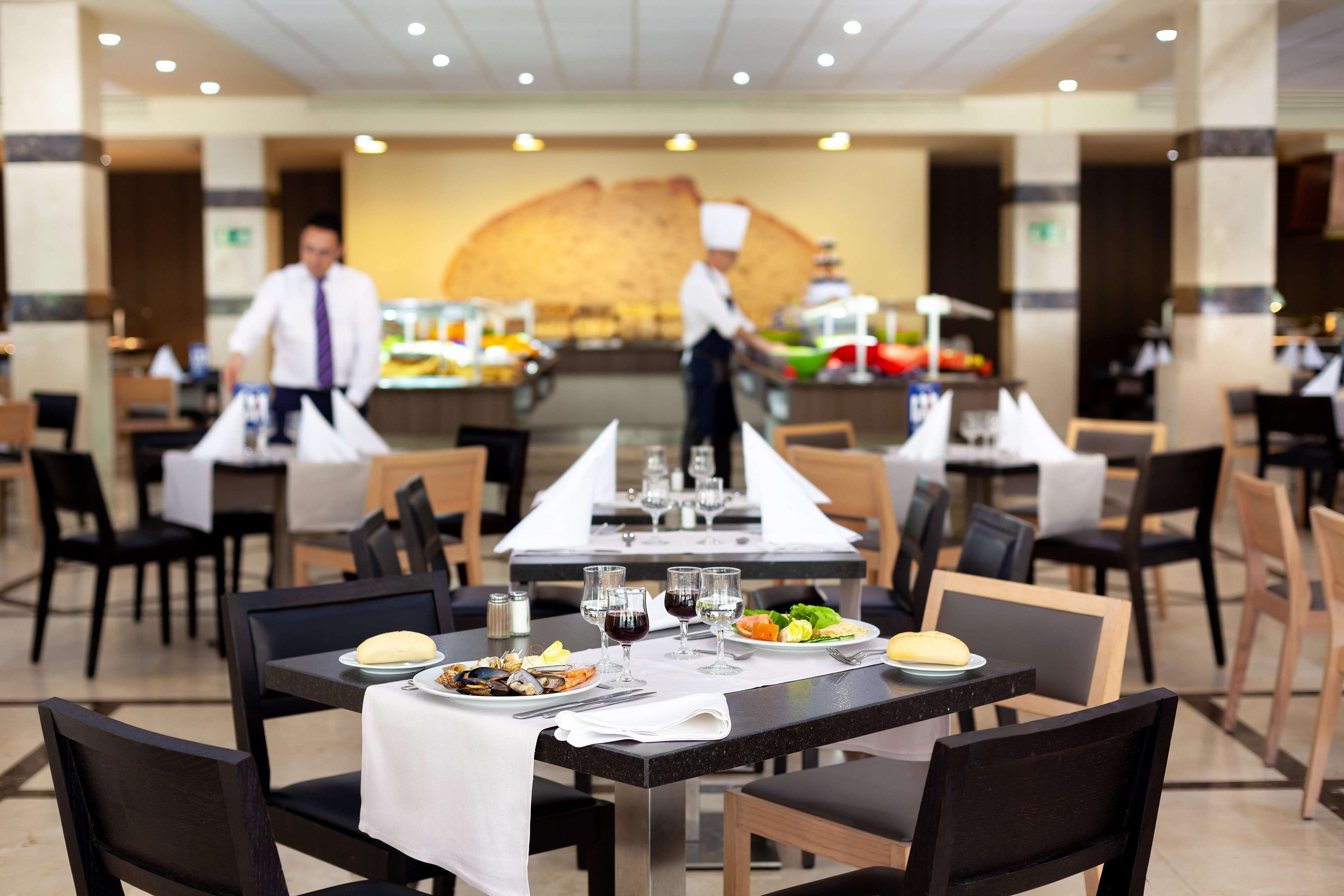 Un comedor de hotel con mesas dispuestas para comidas, un chef al fondo y una barra de buffet.