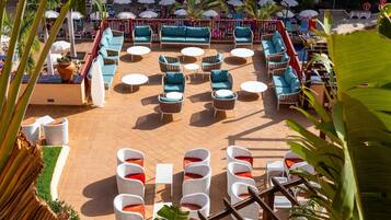 A rooftop terrace with outdoor seating, including sofas and chairs, surrounded by umbrellas and potted plants.