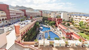 A hotel with multiple swimming pools, outdoor seating areas, and a mountainous backdrop. - Hotel Best Jacaranda (Adeje)