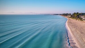 Une plage à l’eau d’un bleu limpide, bordée d’un rivage sablonneux, avec une vue lointaine sur la ville.