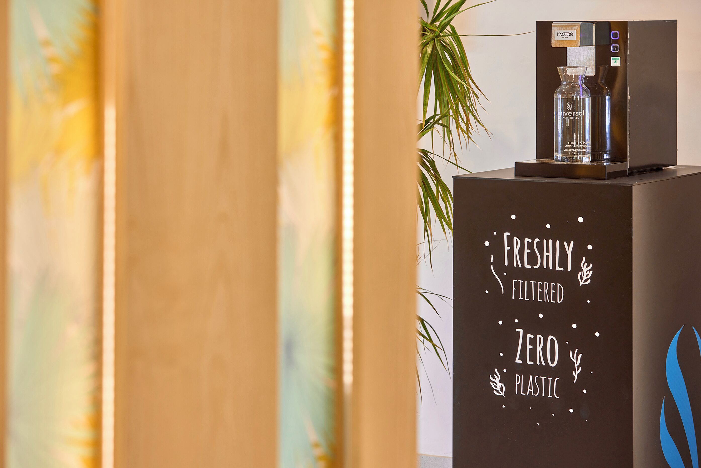 A water dispenser on a counter with a sign stating "Freshly Filtered Zero Plastic."