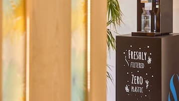 A water dispenser on a counter with a sign stating "Freshly Filtered Zero Plastic."