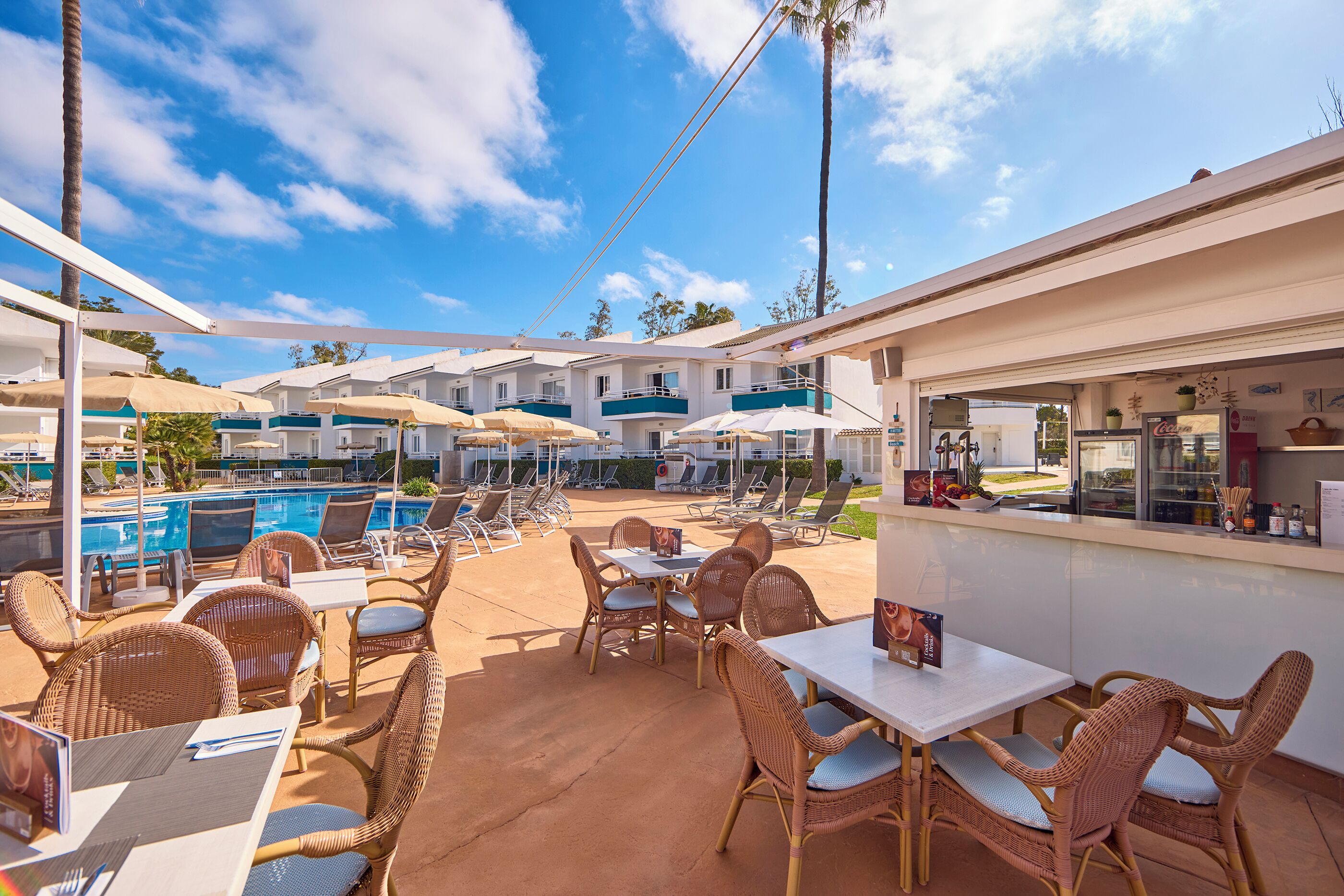 A poolside area with wicker furniture, umbrellas, and a bar counter.