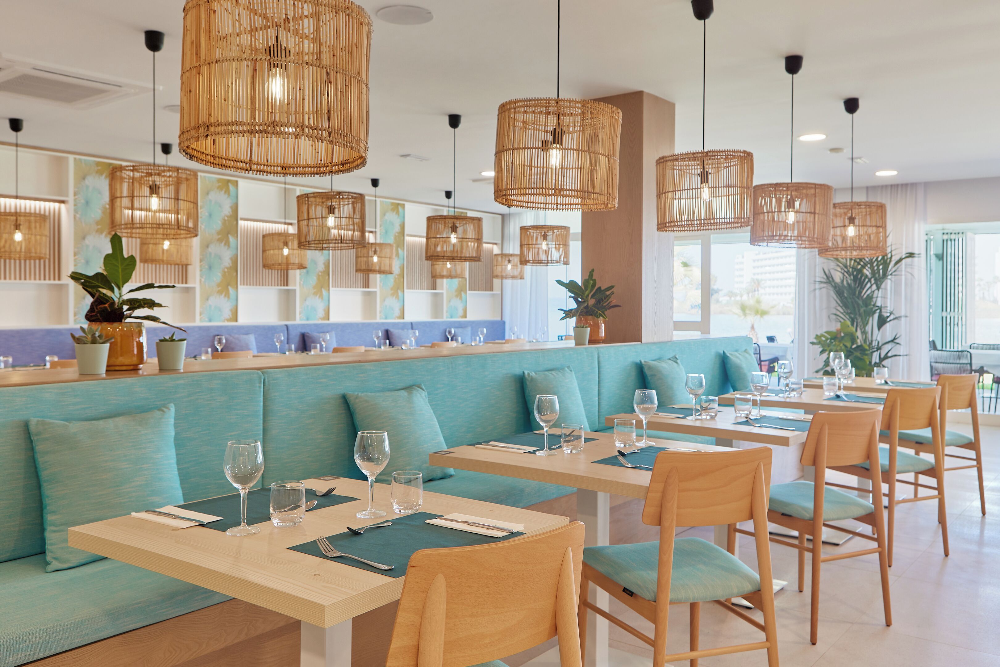 Un restaurante con asientos color turquesa, mesas de madera y lámparas colgantes tejidas.