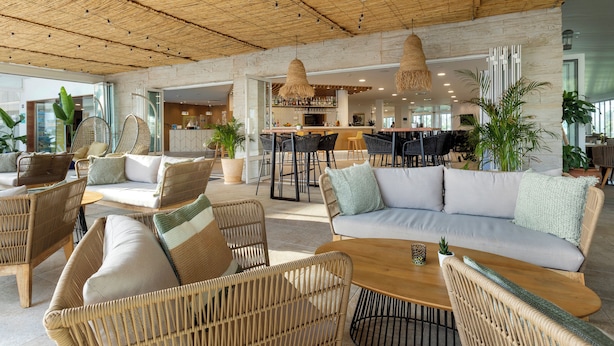 Un espace intérieur spacieux, aménagé avec des meubles en osier, un coin bar et de grandes fenêtres qui laissent entrer la lumière naturelle.