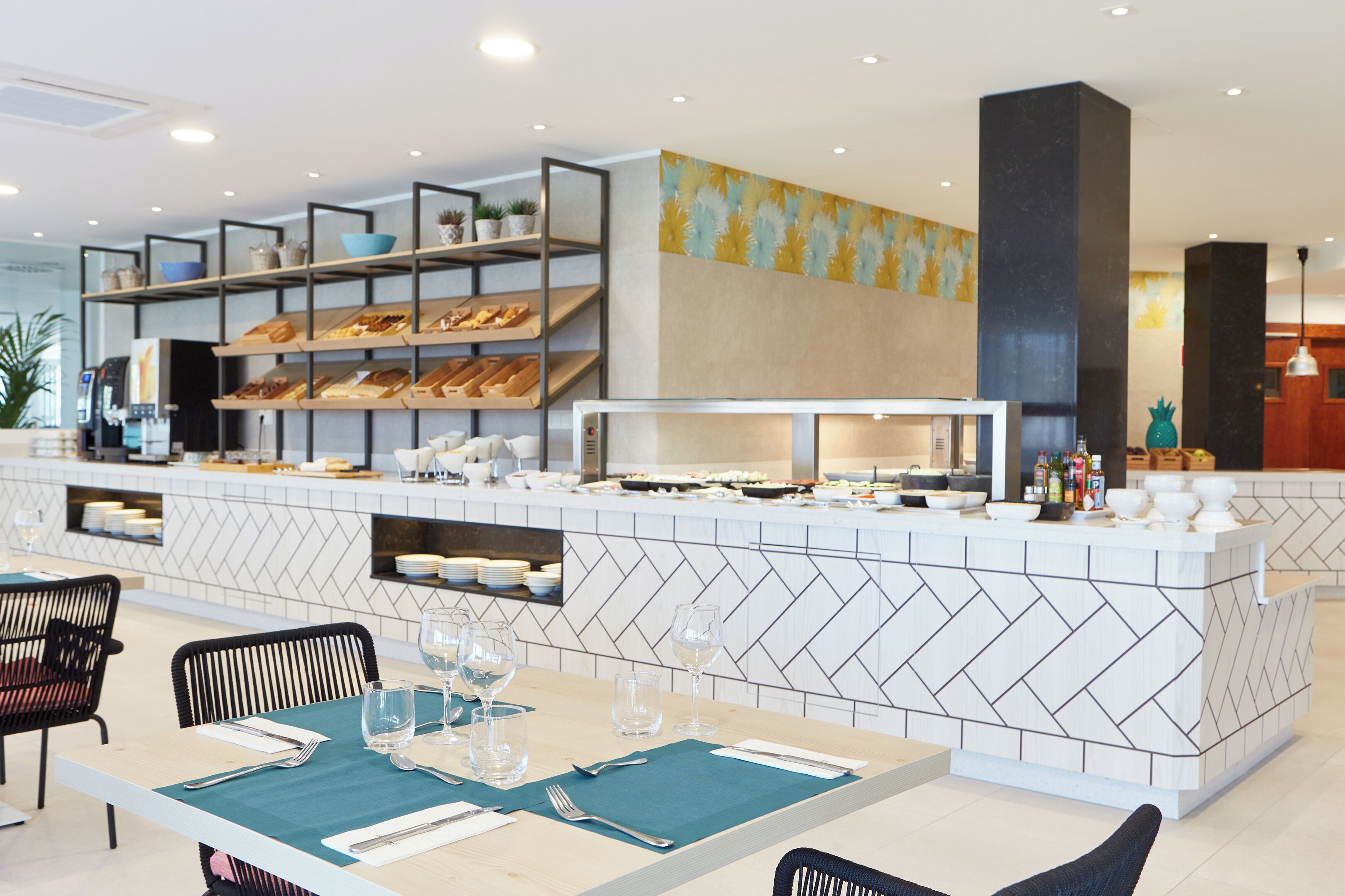 Un restaurante moderno con una barra central, varias áreas de estar y una pared decorativa.