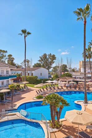 A resort pool area with lounge chairs, palm trees, and a clear blue sky. - Universal Aparthotel Elisa (Muro)
