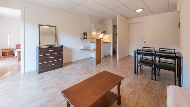 Un vaste espace de vie comprenant un banc en bois, une table à manger avec des chaises, une commode en bois foncé et, au fond, une cuisine.