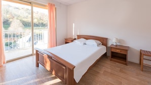 Une chambre d’hôtel avec un lit en bois, une table de chevet, une lampe et une vue sur un balcon doté d’une balustrade.