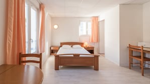 Une chambre à coucher avec un lit en bois, un bureau, une chaise et une table de chevet avec une lampe.