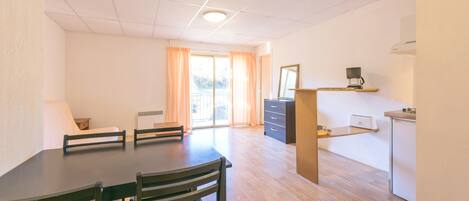 A spacious room with a dining table, chairs, a kitchen area, and a sliding glass door leading to an outdoor balcony.