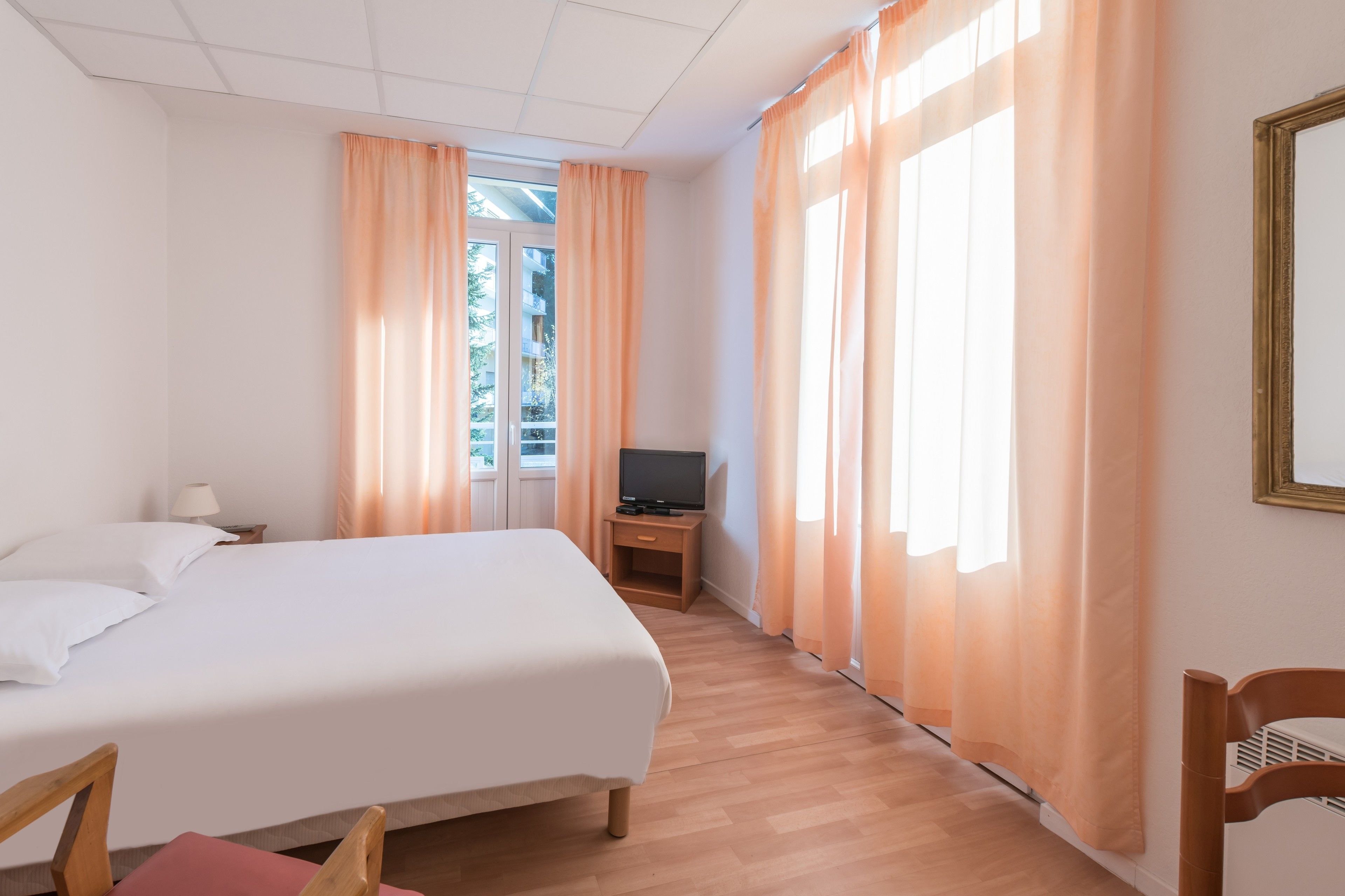 A hotel room with a bed, a TV on a wooden nightstand, and a window with curtains.