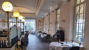Een restaurant met meerdere ronde tafels, kroonluchters en een wijnrek.