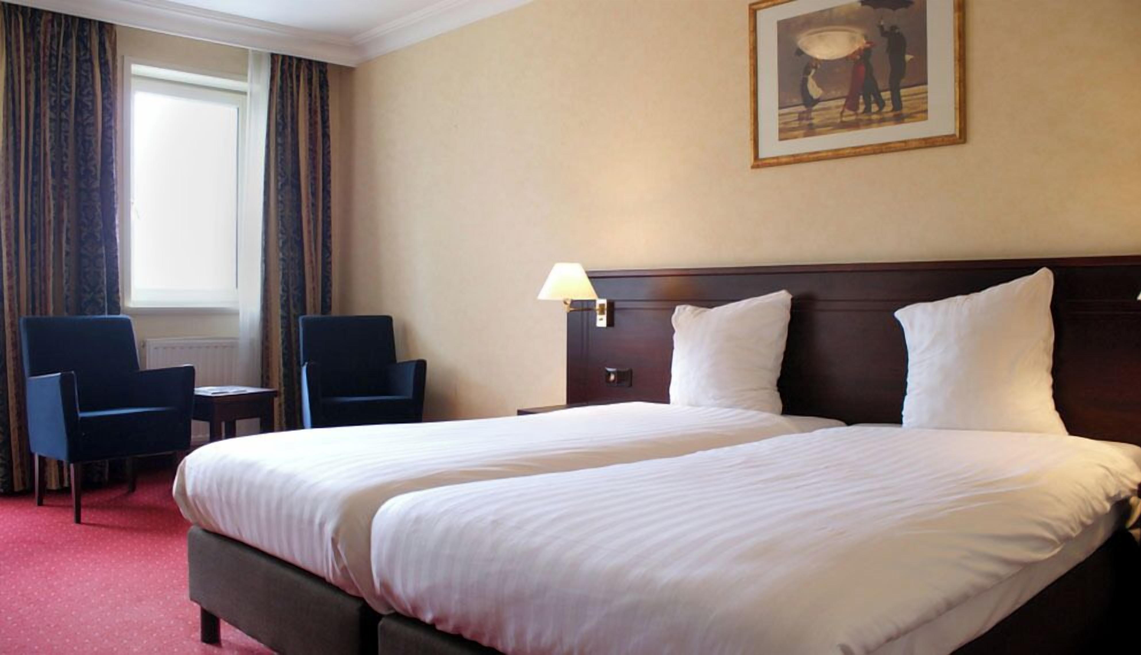 Une chambre d’hôtel avec un grand lit, deux chaises, une table de chevet, une lampe et un tableau au mur.