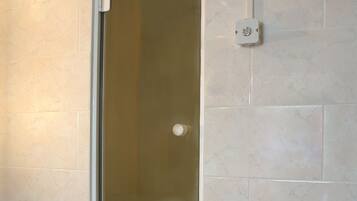 Een badkamer met een douche met glazen wand, betegelde muren en een witte handdoek op de vloer.