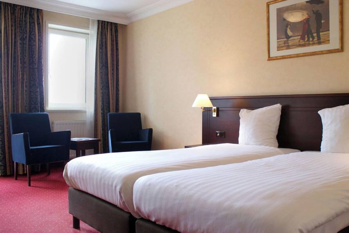 Une chambre d’hôtel avec un grand lit, deux chaises, une lampe et un tableau au mur.