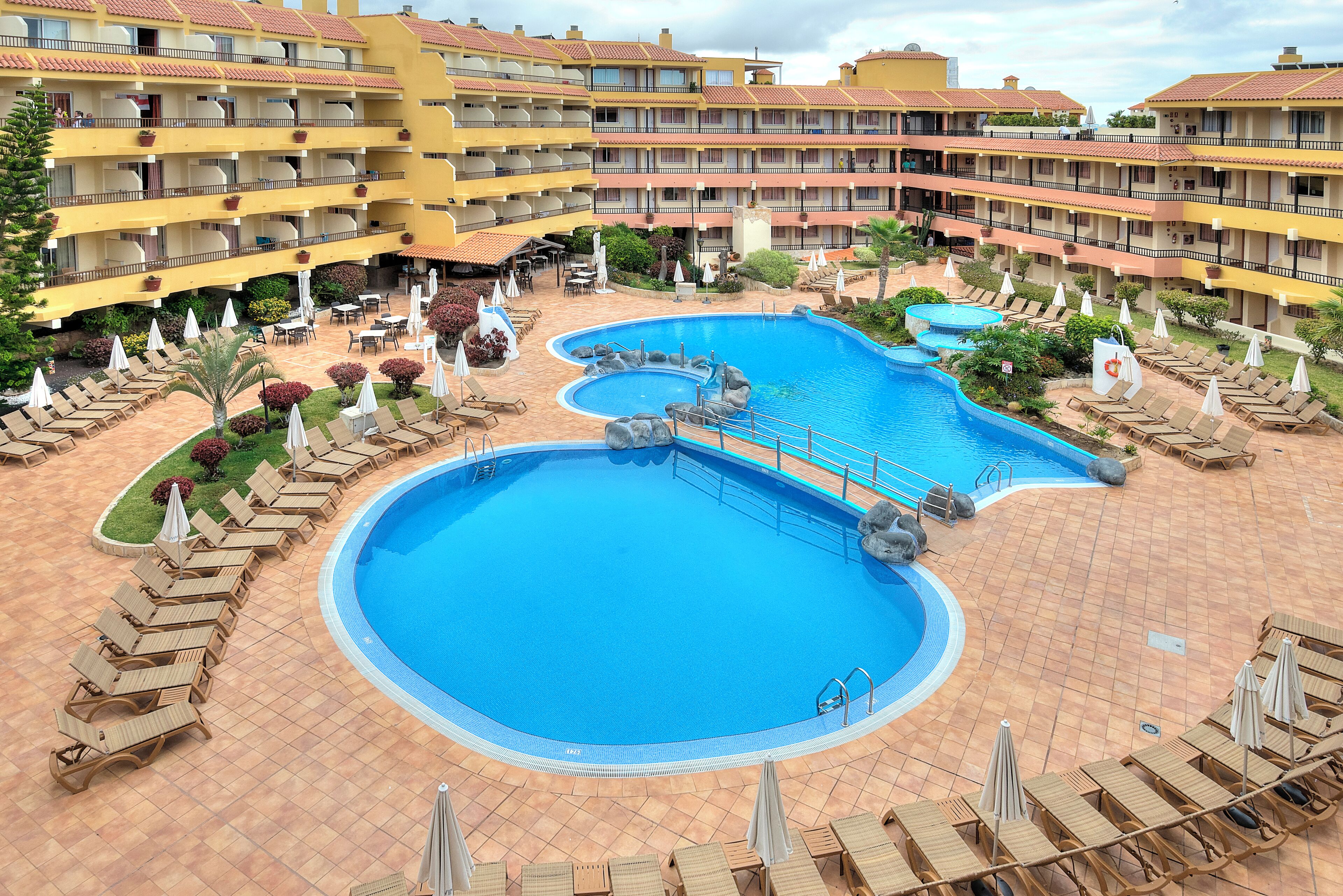 Ein Hotel mit mehreren Balkonen, einem zentral gelegenen Schwimmbad und Liegestühlen.