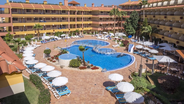 Ein Hotel mit mehreren Schwimmbecken, Liegestühlen und Sonnenschirmen.
