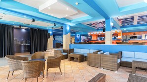 Ein stilvoller Lounge-Bereich mit Rattanmöbeln, einer Bar und Blick auf die Stadt.