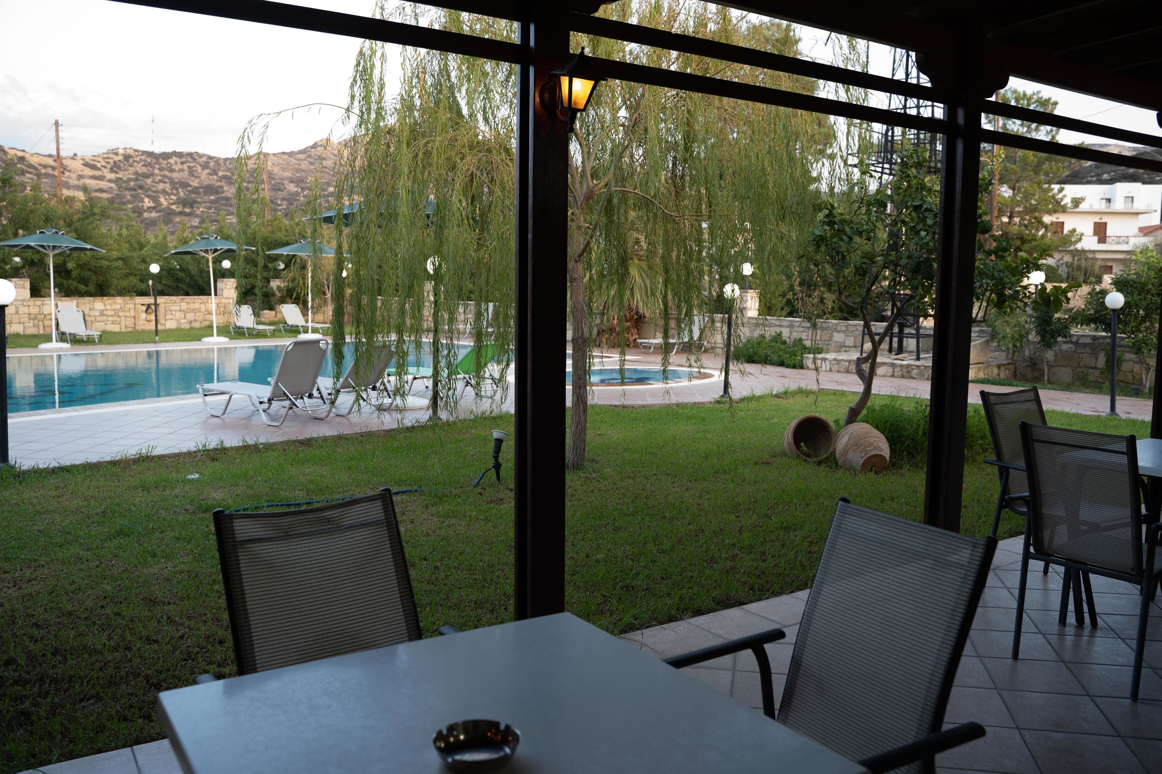 Un área de estar techada al aire libre con vista a la piscina, iluminación exterior y un muro de piedra.