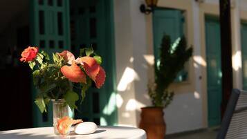 A table with a vase of flowers and a stone, set against a building with green doors and a potted plant.