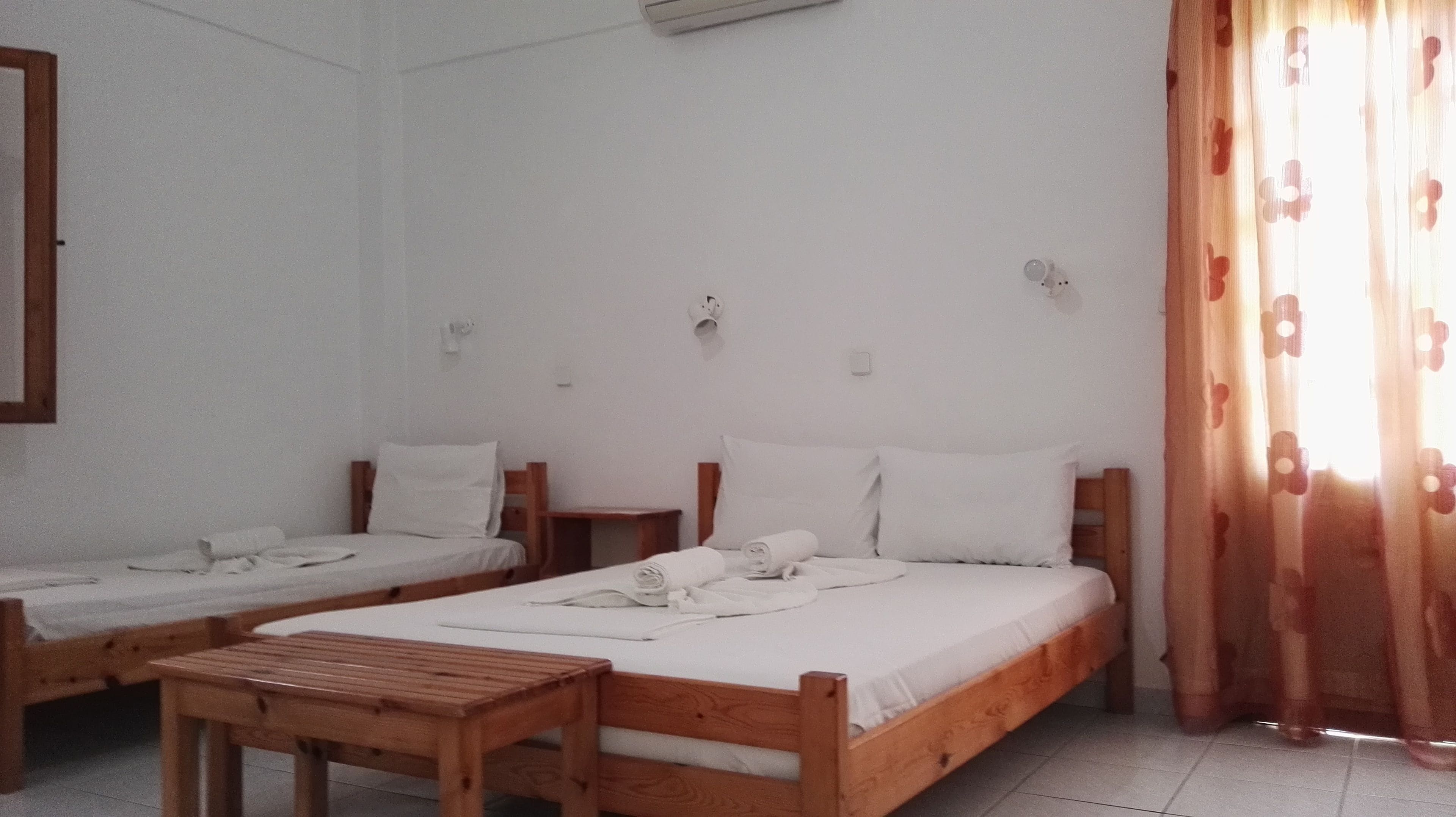 A room with two wooden beds, a small wooden table, and a window with curtains.
